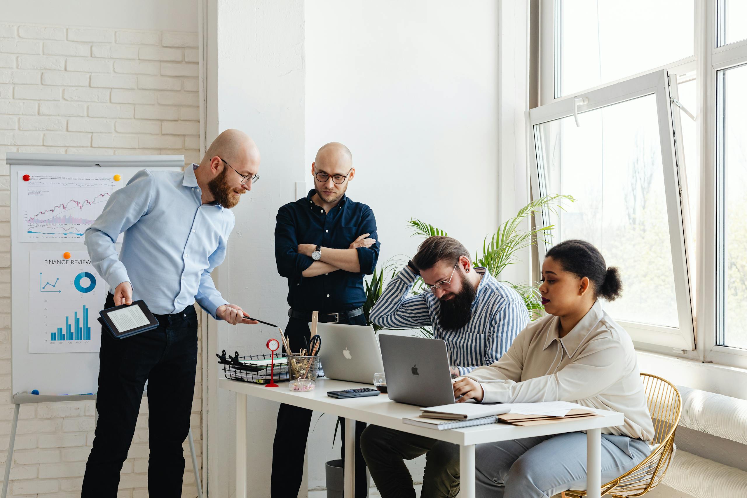 A diverse team discusses strategy in a modern office setting with laptops and charts.