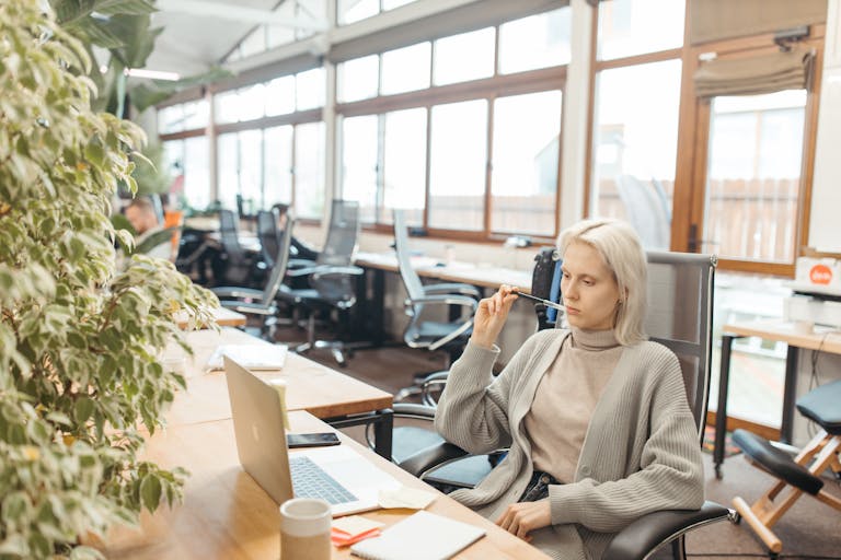A woman thoughtfully works at her desk, embodying focus and professionalism in a modern office setting.
