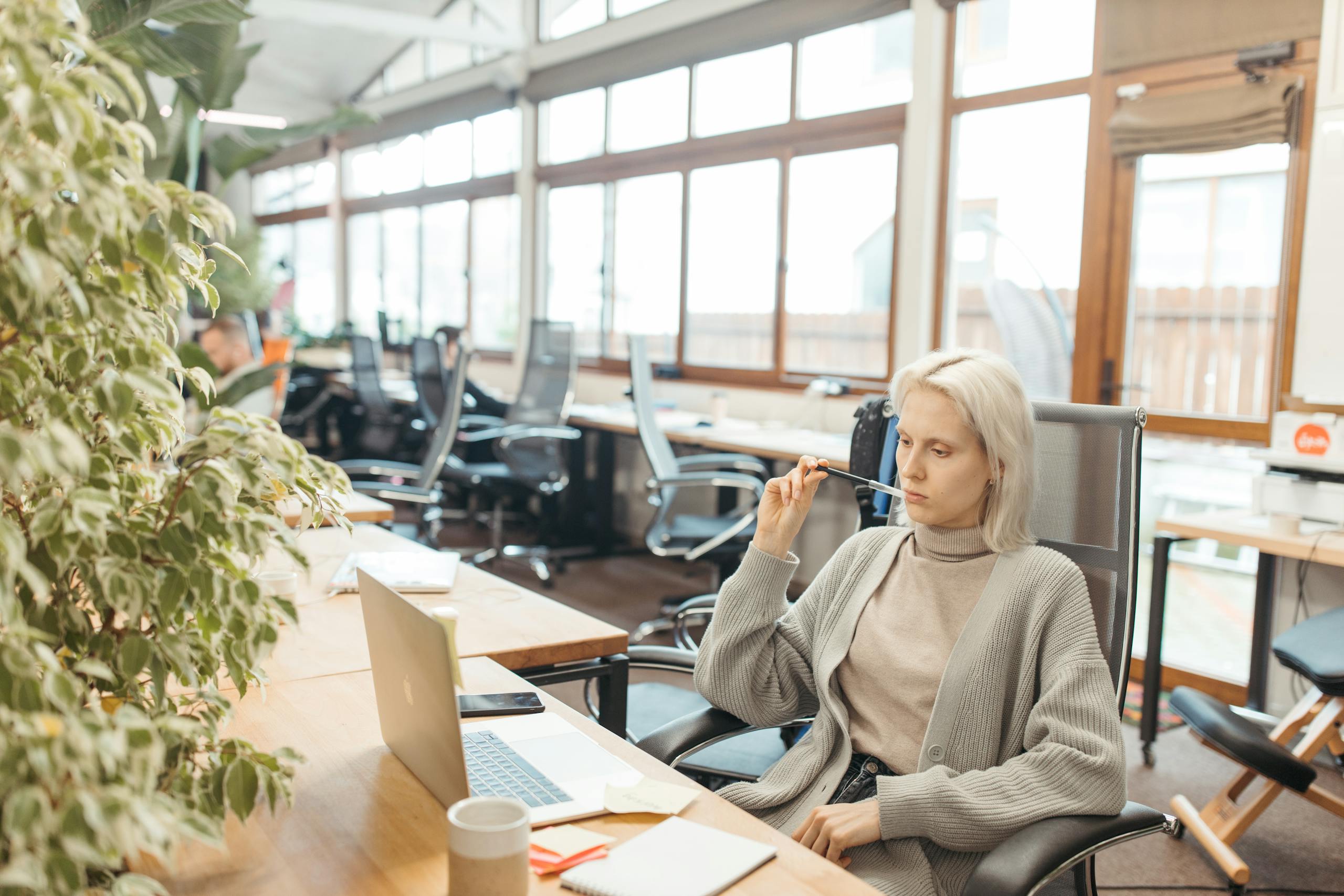 A woman thoughtfully works at her desk, embodying focus and professionalism in a modern office setting.