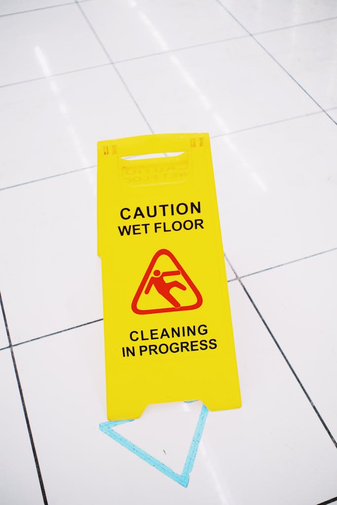 From above of plastic yellow sign with inscription Caution wet floor placed on clean white tiles