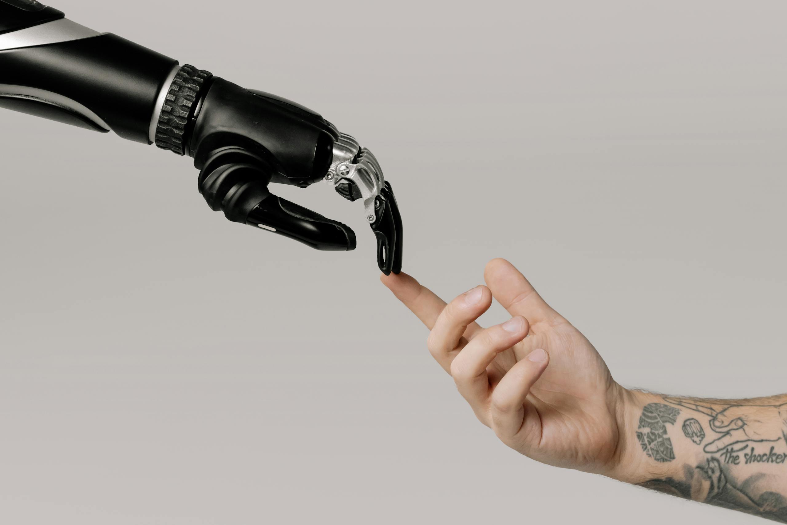 A human hand with tattoos reaching out to a robotic hand on a white background. Référence à l'IA Act